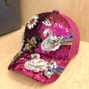 Dettaglio cappellino da baseball rosa con paillettes, decorato con cigno e ape in strass scintillanti.