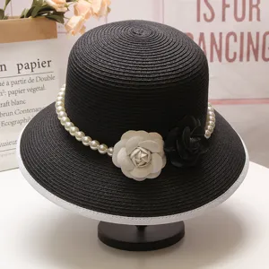 Vue détaillée d'un élégant chapeau de paille noir avec bride de perles et fleurs de camélia.