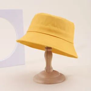 Detail shot of a classic yellow cotton bucket hat on a wooden stand, showing texture and design.