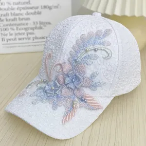 Vista detallada de gorra de béisbol blanca de encaje con bordado floral y detalles de cuentas.