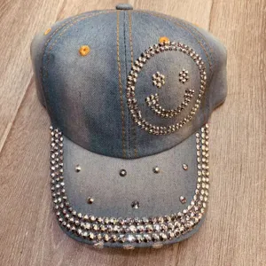 Close-up van lichtblauwe denim honkbalpet met sprankelende strass-smiley en kristallen rand.