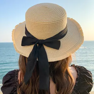Detailed view of a stylish straw sun hat featuring a chic black ribbon bow and frayed wide brim.