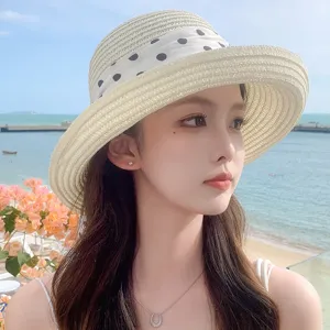 Gros plan d'un chapeau de soleil en paille avec ruban à pois devant un fond de plage