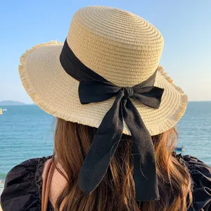 Detail view of a stylish straw sun hat with black bow ribbon against sea backdrop.