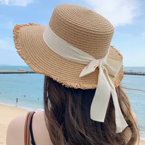 Detail view of a stylish straw sun hat featuring a chic ribbon bow and frayed raw edge brim.