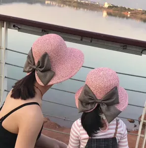 Detail view showing the pink straw sun hat with a grey bow for outdoor summer travel styling.