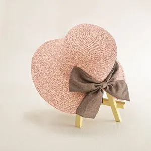 Summer straw hat detail, pink woven texture with elegant grey bow accessory, close up view.