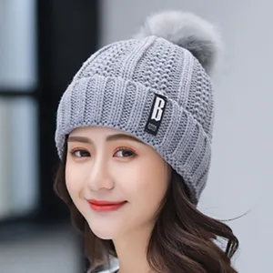 Detail shot of winter fleece-lined knitted hat with fur pom-pom and letter B patch.