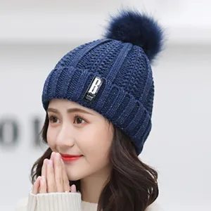 Women's winter warm knitted beanie hat with faux fur pom pom and stylish letter patch.