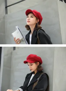 Close-up detail shot of a stylish red wool octagonal beret hat worn by model against grey wall.