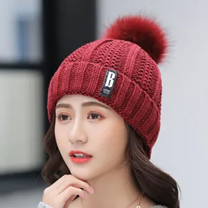 Detailed view of a stylish red knitted winter hat featuring a fluffy pom pom and front label.
