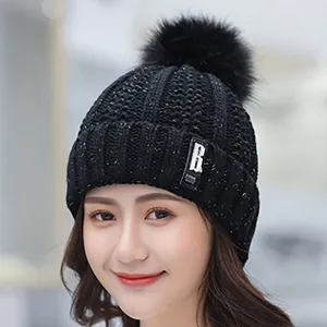 Close-up of black knitted winter beanie with gold flecks, fluffy pom-pom, and side tag.