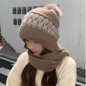 Brown knitted beanie with integrated scarf and fluffy pom-pom, cozy winter accessory.