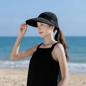 Detail view of a black empty-top sun visor with wide brim, worn by a model at the sunny beach.