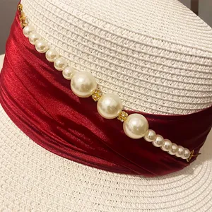 Detail view of summer French elegant straw hat with red ribbon and white pearls.
