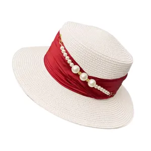 Close-up detail of white straw hat with red ribbon and elegant pearl bead strand decoration.