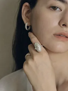 Detailed view of vintage silver textured oval ring and hoop earrings on a model.