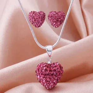 Makroansicht des funkelnden rosa kristallbesetzten Herzanhängers und der Ohrringe