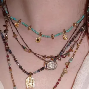 Primer plano de collares en capas con cuentas de turquesa, turmalina y dijes dorados.