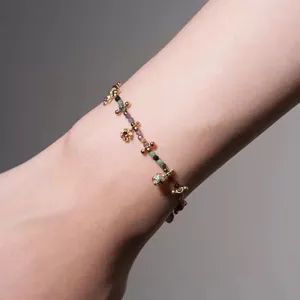 Detalle de una pulsera de cuentas de turmalina de colores con delicados dijes de flores doradas.