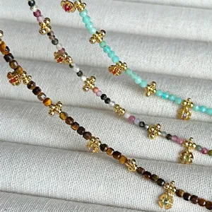Primer plano de collares de piedra natural con trébol dorado y colgantes de flores