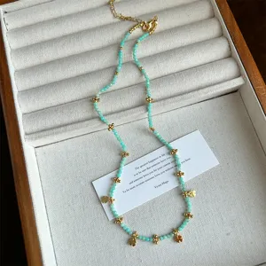 Vista detallada de collar de cuentas verde turquesa con colgantes de trébol dorados
