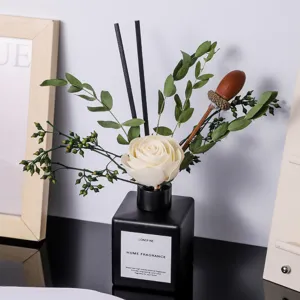 Difusor de aromas de vidrio negro con flor de madera blanca y plantas verdes para el hogar.