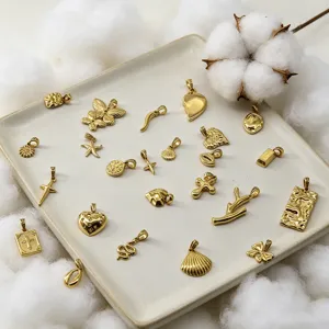 Draufsicht auf verschiedene 18K vergoldete Edelstahlanhänger auf einem Keramiktablett.