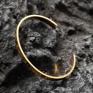 Minimalist gold-plated stainless steel open cuff bracelet for men on stone texture.