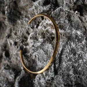 Close-up detail of minimalist gold-plated stainless steel cuff bracelet on rough stone