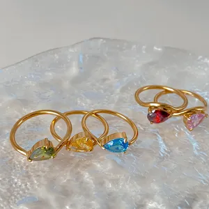 Close-up view of elegant gold rings with colorful pear-shaped zircon stones on textured glass