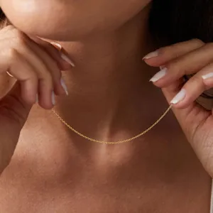 Vue détaillée d'un collier chaîne fine minimaliste en acier doré sur le cou.