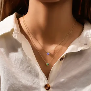 Detail of layered gold birthstone necklaces with purple and green round crystal pendants