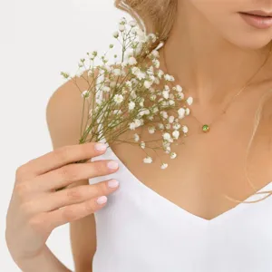 Elegant gold necklace featuring a green birthstone pendant worn by a model