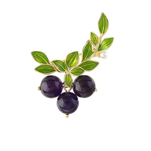 Primer plano de un elegante y delicado broche de arándano con hojas doradas y bayas moradas.