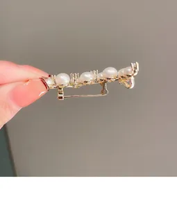 Close-up detail of the elegant gold-tone pearl brooch pin showing the secure metal clasp.