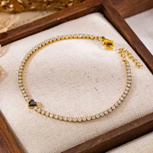 Gedetailleerd overzicht van gouden tennisarmband met witte zirkoon en zwart hartje