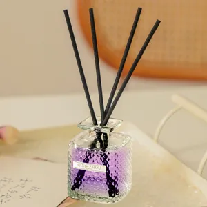 Close-up detail of glass diffuser bottle with purple liquid and black reed sticks.