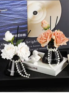 Detailed view of luxury aroma diffuser with artificial roses and pearls in black vase.