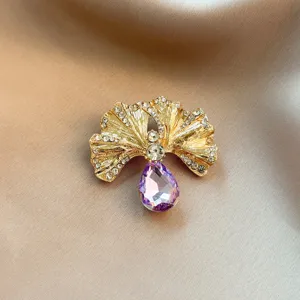 Close-up detail of a gold ginkgo leaf brooch featuring sparkling rhinestones and purple crystal.