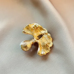 Close up back detail of elegant gold ginkgo leaf brooch with pin and pearl charm.