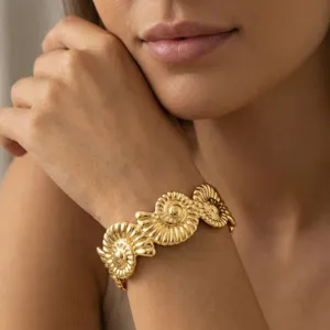 Nahaufnahme eines floralen, vergoldeten Edelstahl-Armreifens am Handgelenk des Models