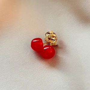 Vue en gros plan d'une broche cerise rouge élégante avec tige dorée sur fond de tissu.