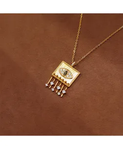 Detailed shot of a gold square pendant with an evil eye and dangling cubic zirconia charms.