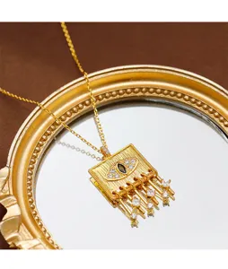 Detailed view of gold evil eye square pendant with zircon tassels on a mirror.