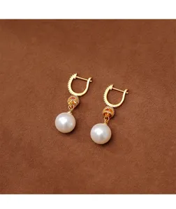 Detalle de elegantes pendientes de perlas blancas con clips de oreja dorados y circones