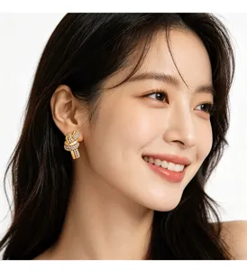 Close-up of designer gold knot stud earrings with crystals worn by a smiling model.