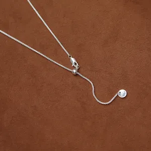 Elegante verstelbare zilveren ketting met schuifsluiting op bruine achtergrond.