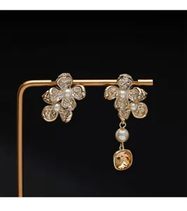 Detalle de pendientes asimétricos de flores doradas con perlas y gema color ámbar