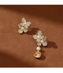Vista detallada de pendientes florales asimétricos dorados con perlas blancas y piedras ámbar.